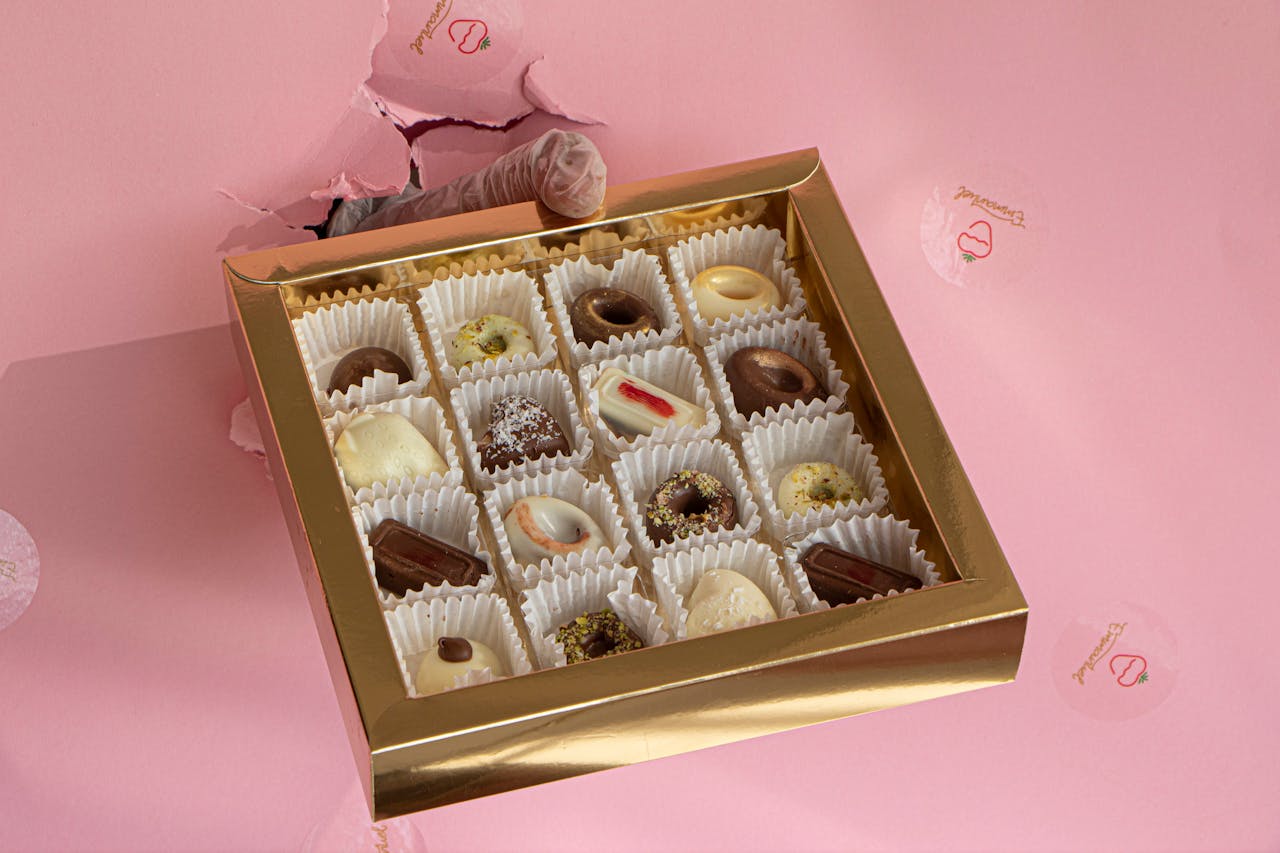 Luxurious assorted chocolates beautifully arranged in a gold box on a pink background.